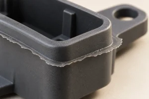 Close-up illustration of a molded plastic housing with a thin fin of flash extending along its parting edge.
