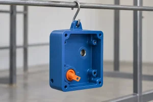 Illustration of a blue-coated metal housing suspended from a finishing rack with an orange masking plug in one bore.